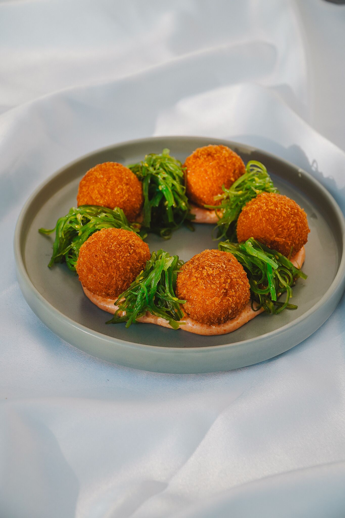 Un plato con tres porciones redondas y empanizadas, y adorno verde sobre un plato gris.