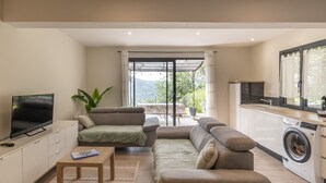 A modern living room with a flat-screen TV, a sofa, a coffee table, and a washing machine. - Apartment "Gîte les Monteils" with Mountain View, Private Terrace & A/C (Vesseaux)