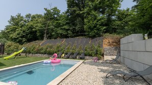 A swimming pool with lounge chairs, a slide, and a stone wall. - Apartment "Gîte les Monteils" with Mountain View, Private Terrace & A/C (Vesseaux)