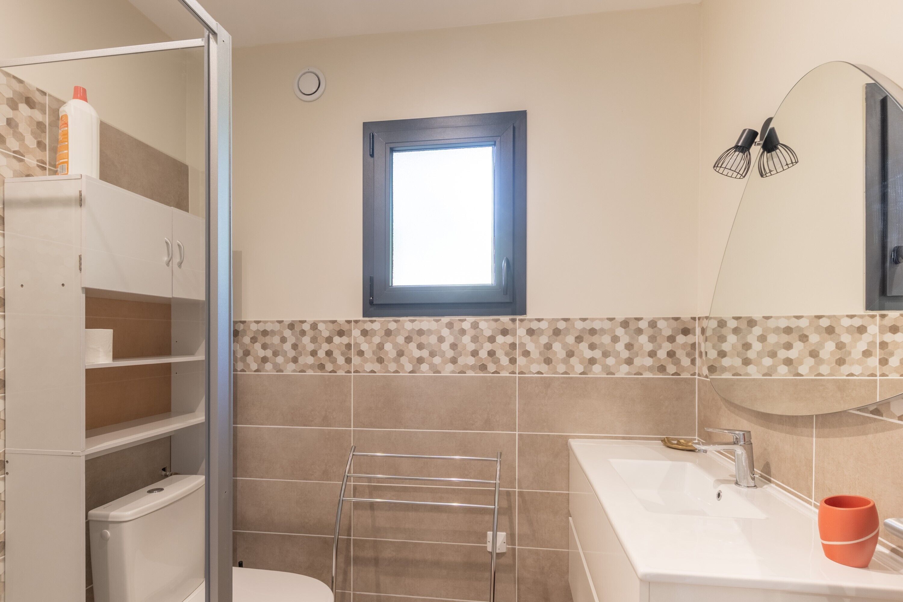 Une salle de bain équipée de toilettes, d’un lavabo, d’un porte-serviettes et d’une fenêtre donnant sur un paysage agréable.
