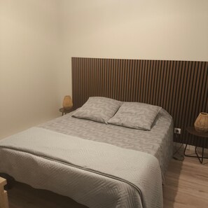 A neatly made bed with a patterned bedspread and pillows, a bedside lamp, and a wall with vertical wooden slats. - Apartment "Gîte les Monteils" with Mountain View, Private Terrace & A/C (Vesseaux)