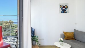 Ett modernt vardagsrum med en grå soffa, ett litet vitt bord och en röd stol. Det hänger en tavla på väggen och en krukväxt står på golvet.