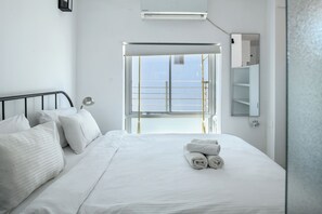 A modern hotel room with a large bed, white linens, a bedside table with a lamp, a window with a view, and a mounted TV. - Grand STU SeaView Balcony by Sea N' Rent (Tel Aviv)