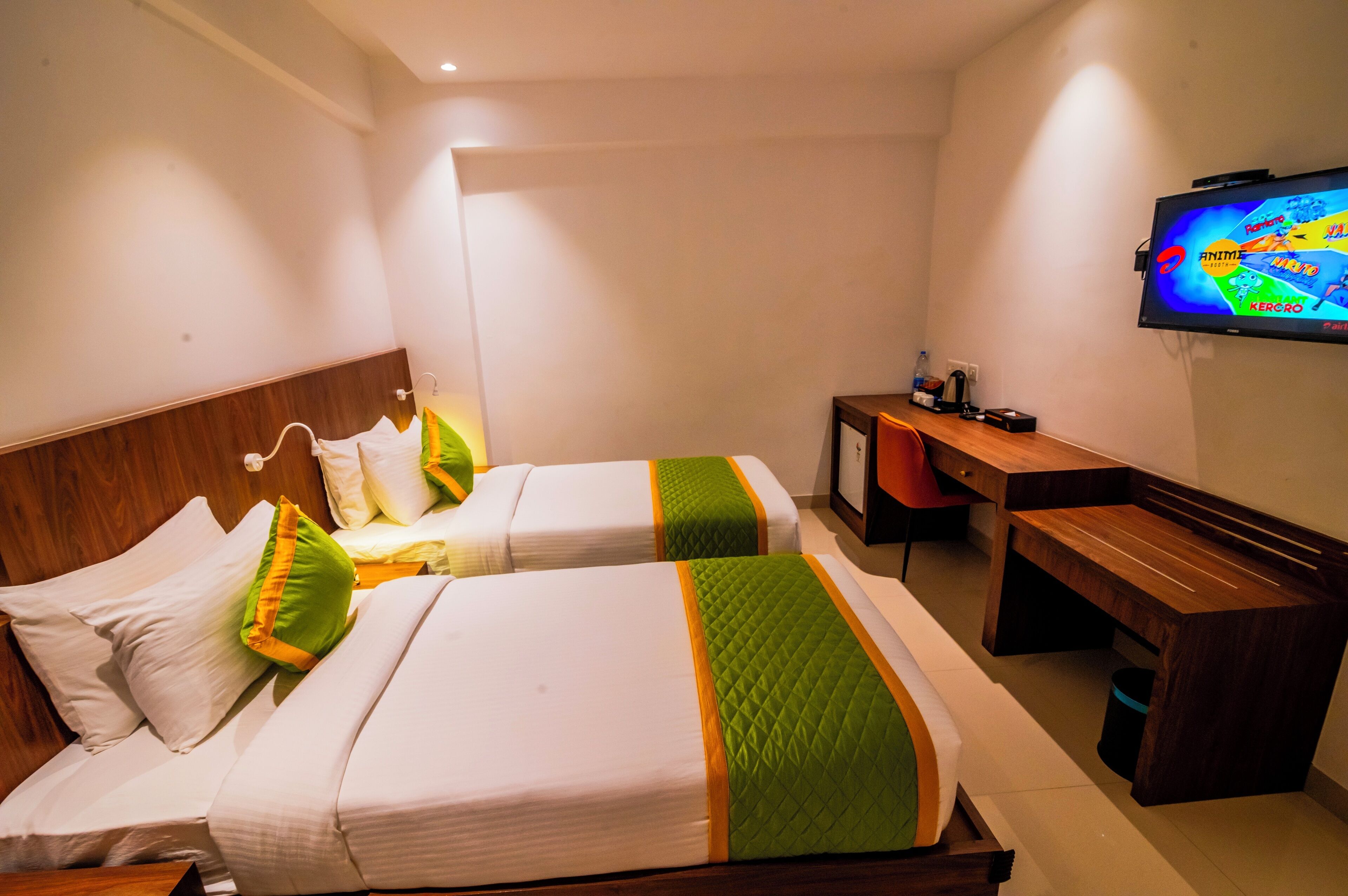 A hotel room with two beds, a desk, a TV, and a trash bin.