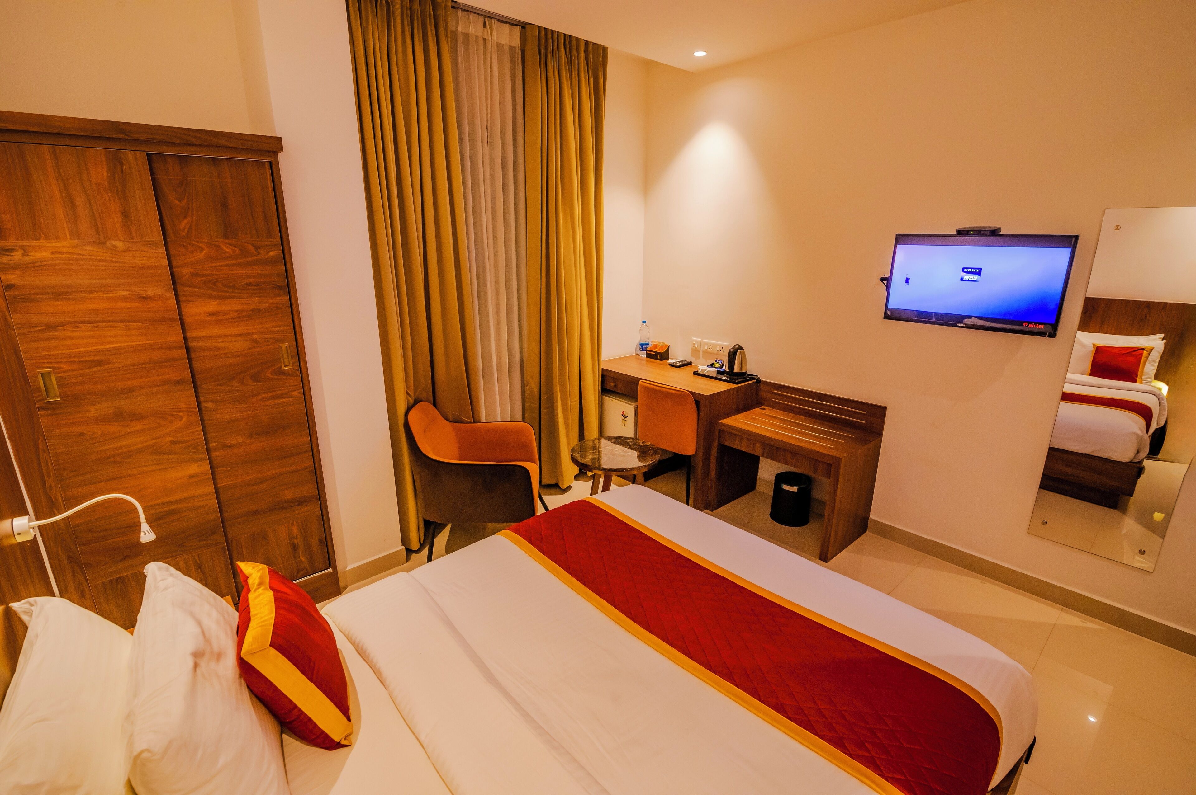 A hotel room with a bed, a desk, a chair, a television, and a wardrobe.