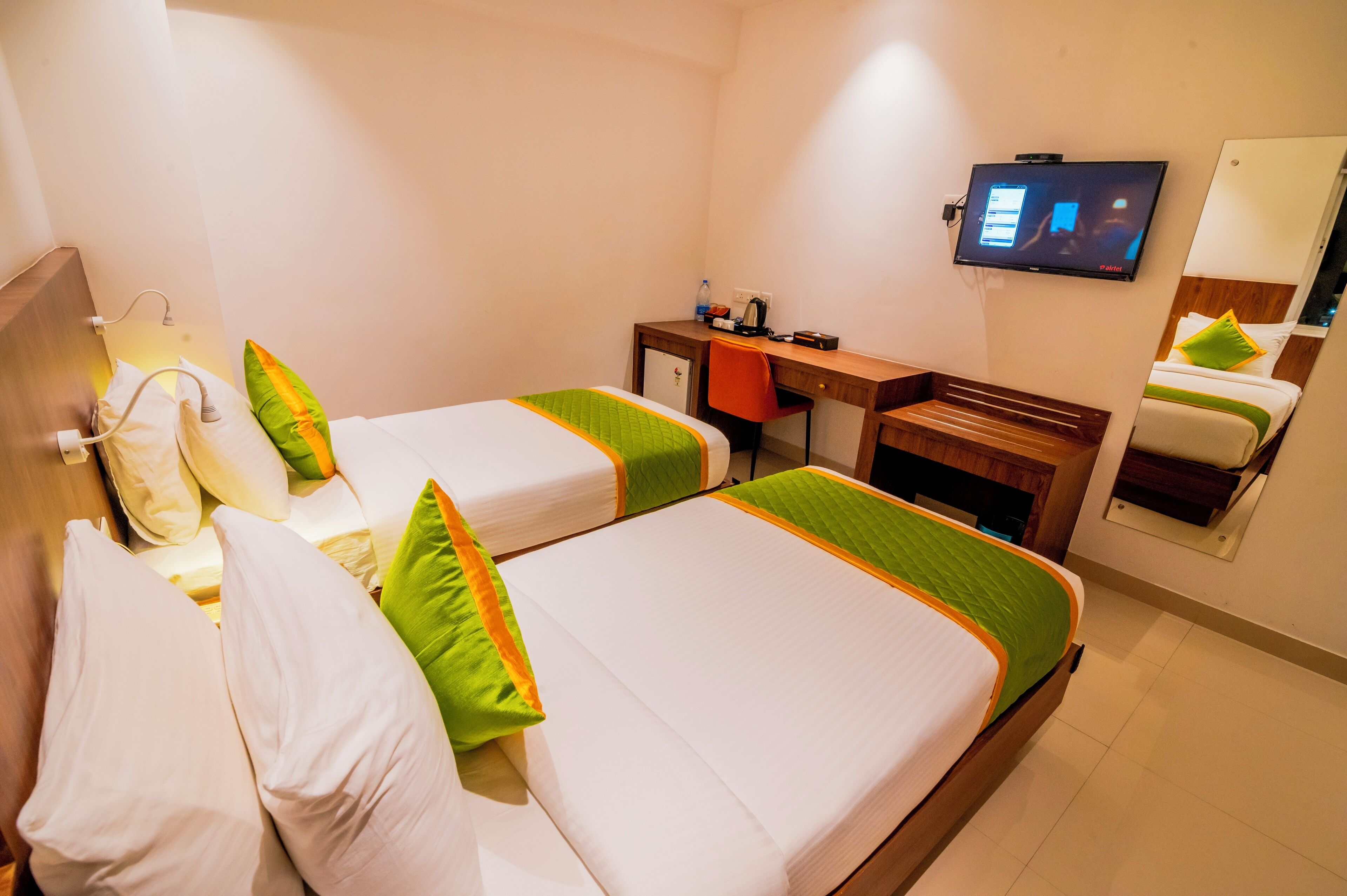 Een hotelkamer met twee bedden, een bureau, een televisie en een spiegel.