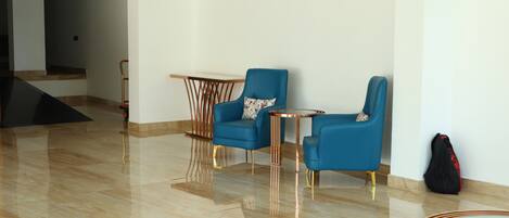 Una habitación amplia con suelo de mármol pulido, un sofá azul, una mesita redonda y una mesa de centro moderna.