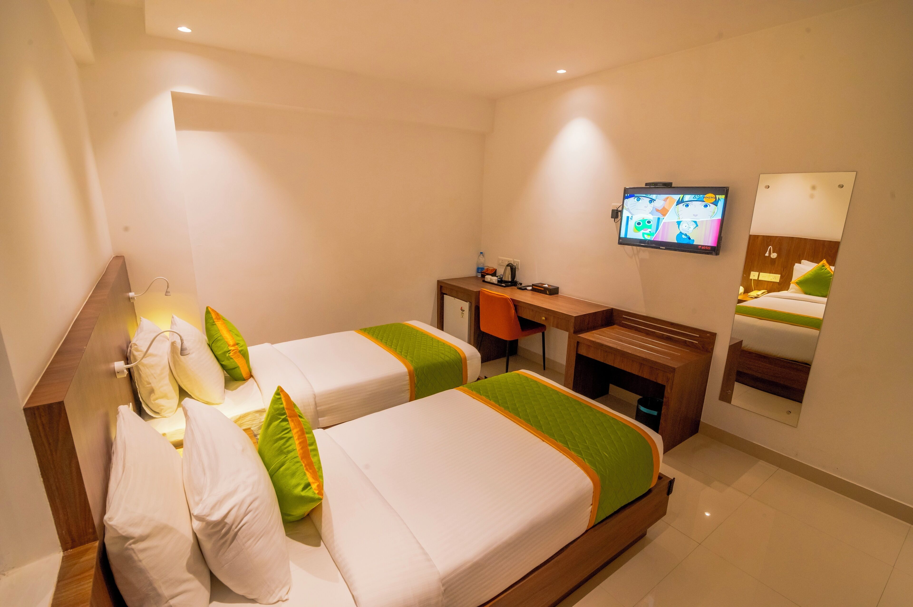 Una habitación de hotel con dos camas, un escritorio, una silla, un televisor y un espejo.