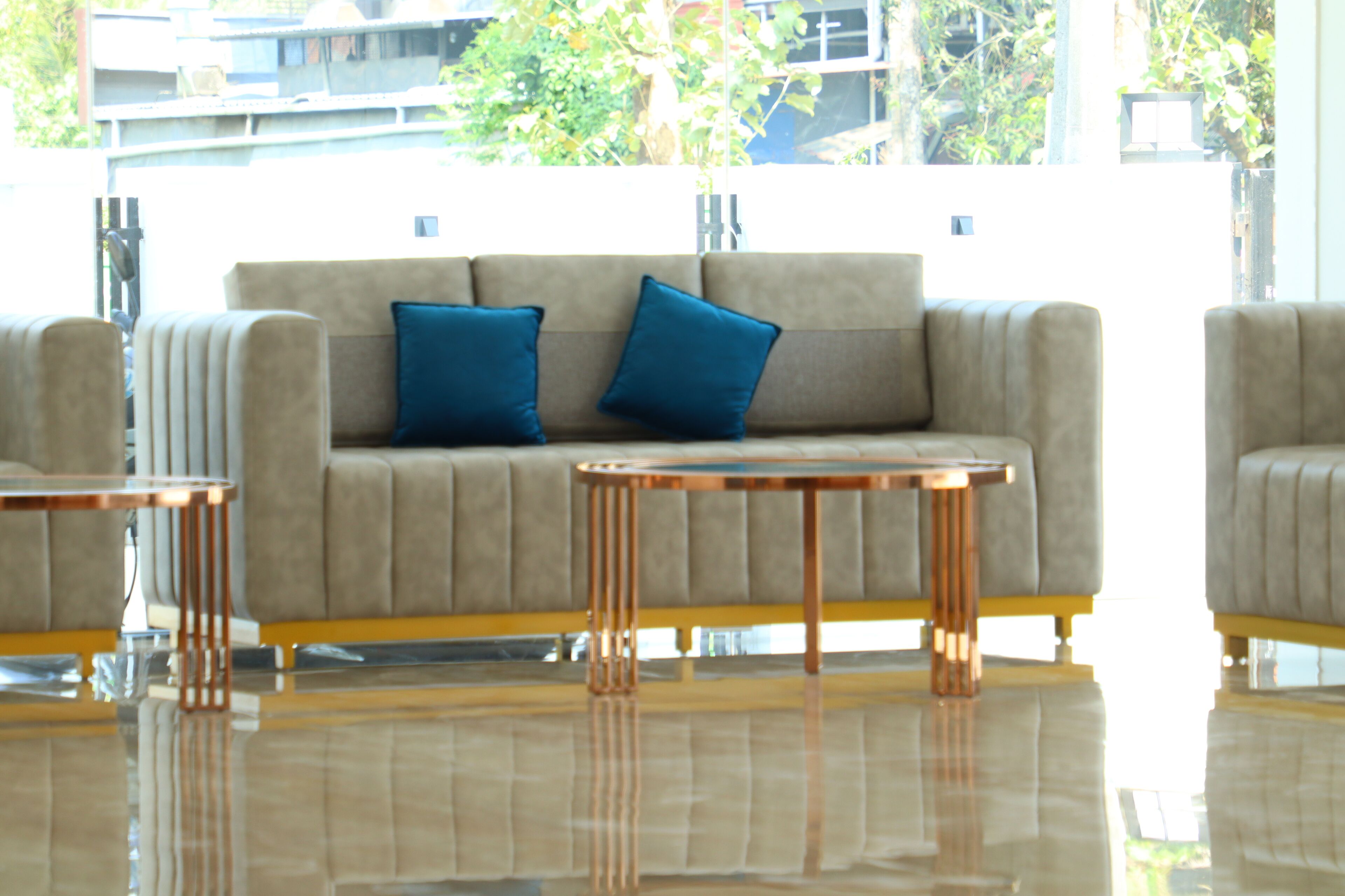 A modern living room with a beige sofa, two blue cushions, and a glass coffee table.