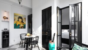 A modern hotel room with a checkered floor, a dining area with a table and chairs, a large painting, a black door, and a bed with a green pillow. - Villa Martini Beachside 4 (Canggu)
