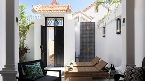 A sunlit courtyard with a black door, wicker furniture, and a tiled wall. - Villa Martini Beachside 4 (Canggu)