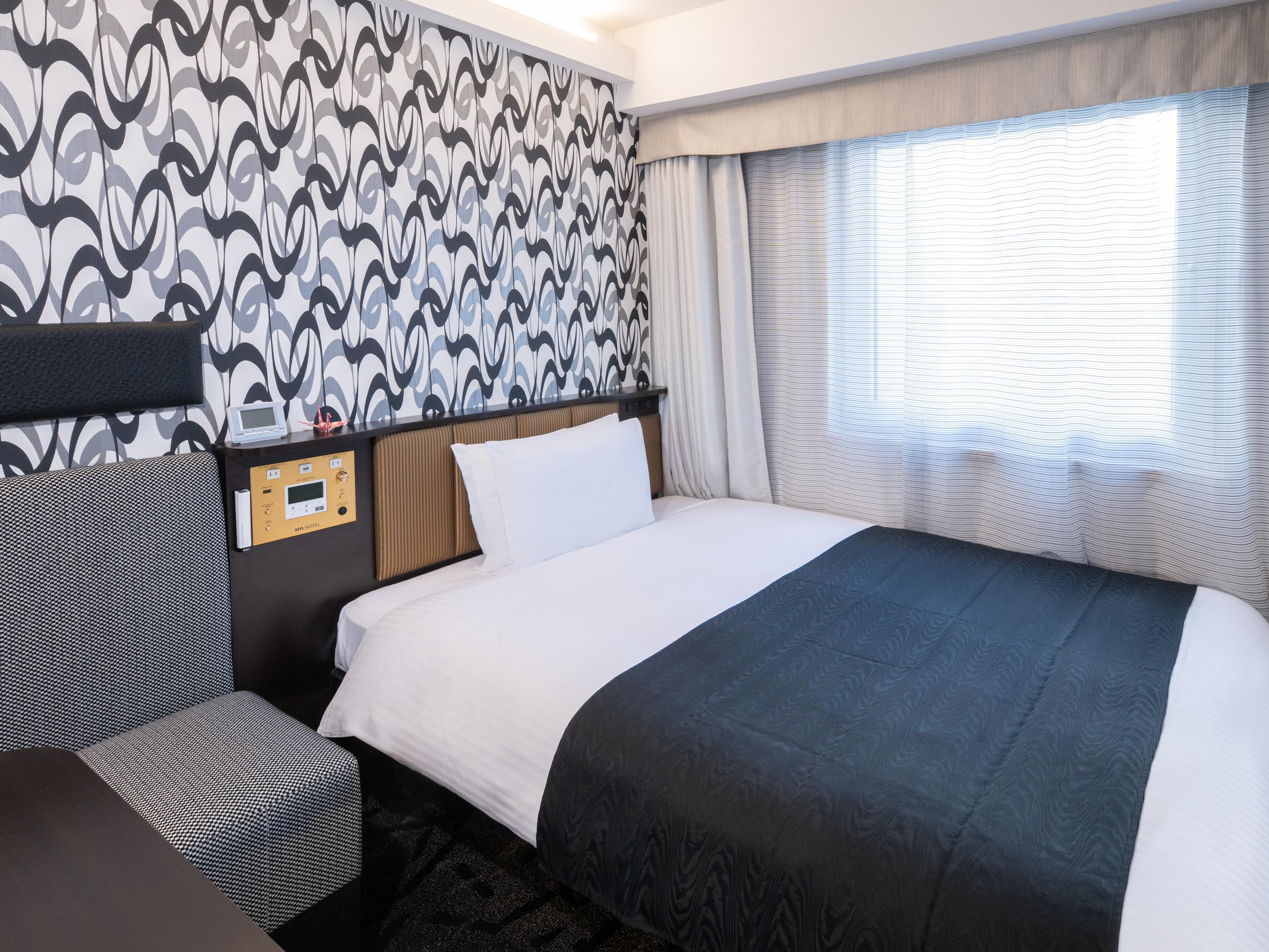 Quarto de hotel com cama, painel de controle, cabeceira, mesa de cabeceira e janela com cortinas.