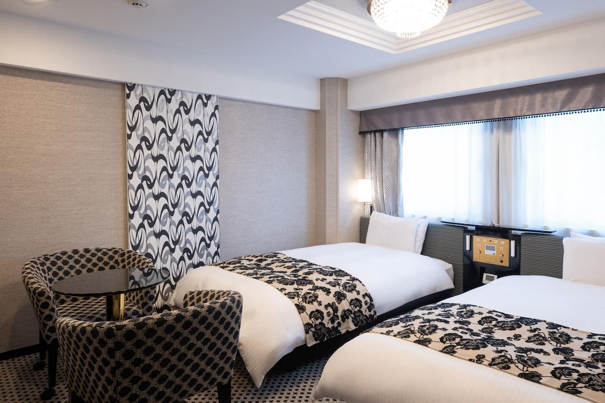 A hotel room with two beds, a small table, and a chair.