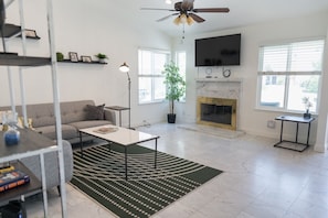 A modern living room with a sofa, coffee table, fireplace, TV, and a ceiling fan.