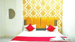 Habitación de hotel con cama, almohadones rojos, manta roja, control remoto y un espejo en la pared.
