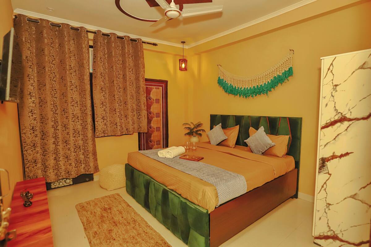 A bedroom with a bed, curtains, a ceiling fan, a wall decoration, and a bedside table.