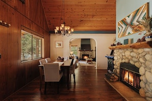 A dining area with a stone fireplace, wooden ceiling, and a view through an arched doorway.