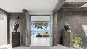 Un intérieur moderne donnant sur la mer grâce à une porte ouverte, des murs en marbre et deux sculptures posées sur des piédestaux.