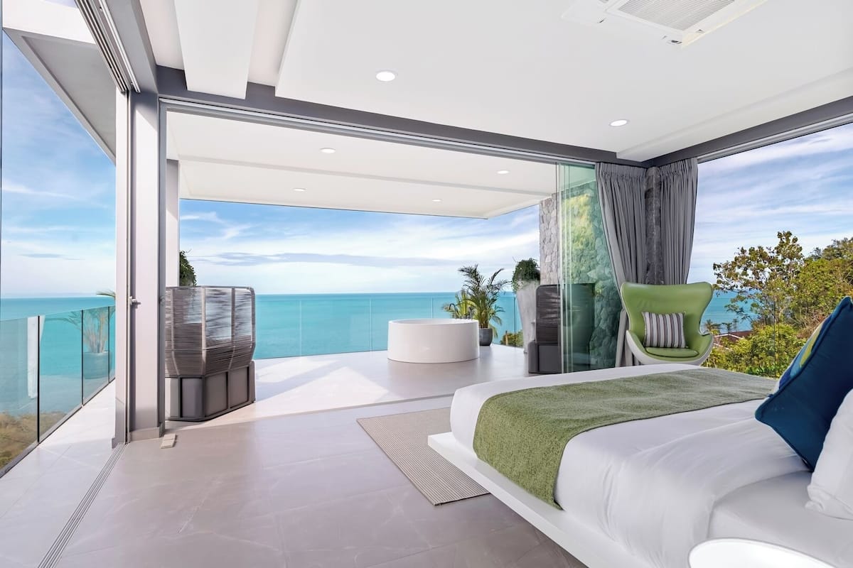 Ein modernes Schlafzimmer mit einem großen Bett, einer Sitzecke und Blick auf den Ozean.