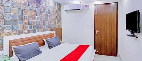 A bedroom with a bed, a wall-mounted air conditioner, a wooden door, and a television on the wall.