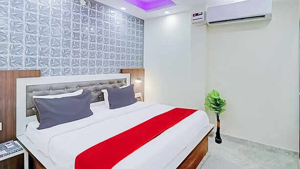 A hotel room with a bed, a nightstand, a wall-mounted air conditioner, and a ceiling with purple lighting. - Roomshala 089 Green Palace (New Delhi)