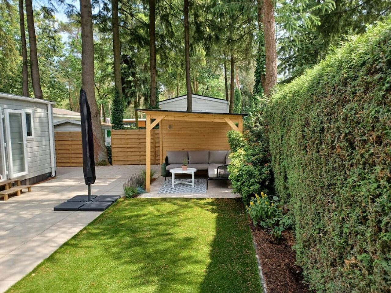 Ein Garten mit einer Holzterrasse, einer überdachten Sitzgelegenheit und einem Rasen.
