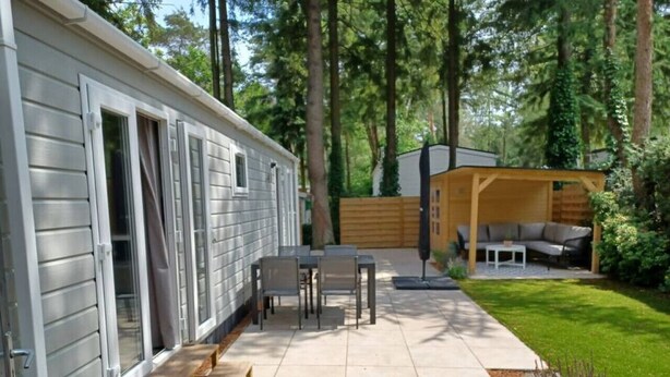 A mobile home with a patio area, including a table and chairs, a wooden deck, and a covered seating area. - Cottage with a large garden (Hoenderloo)