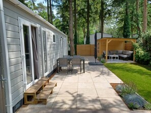 Une maison mobile dotée d’un espace patio comprenant une table et des chaises, une terrasse en bois et un coin salon couvert.