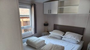A neatly made bed with white linens and pillows, a bedside lamp, and a window with curtains. - Cottage with a large garden (Hoenderloo)