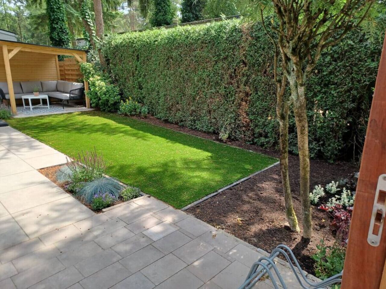A well-maintained garden with a lawn, a wooden pergola, and a seating area.