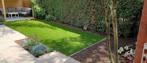A well-maintained garden with a lawn, a wooden pergola, and a seating area.
