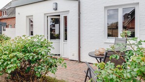 Une maison en briques blanches avec une porte, des fenêtres et un petit patio comprenant une table et des chaises.