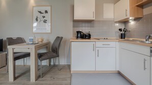 Une cuisine moderne avec des meubles blancs, un plan de travail en bois et un coin repas comprenant une table et des chaises.