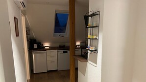 En smal hall leder in till ett kök med vita skåp, en diskmaskin och ett fönster ovanför diskbänken.