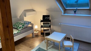 Ett litet, ombonat rum med en säng, ett skrivbord och en stol. Det finns ett fönster med utsikt över himlen och ett element på väggen.