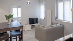 Uma sala de estar moderna com um sofá, uma televisão, uma mesa de jantar e uma planta.