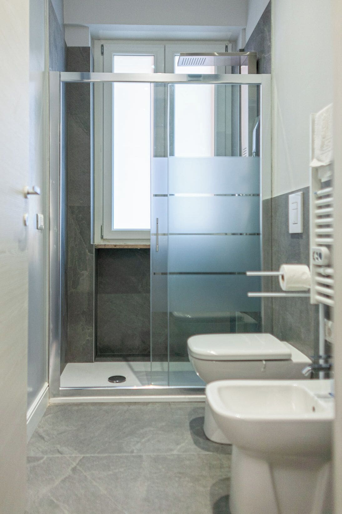 A modern bathroom with a glass shower enclosure, a toilet, and a bidet.