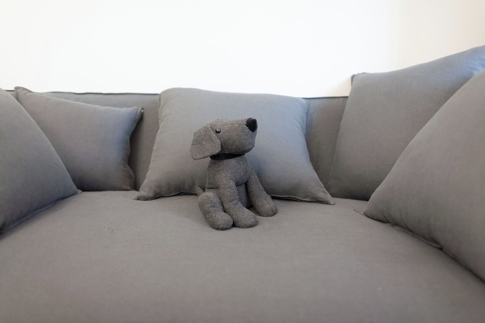 A grey sofa with a grey cushion and a grey stuffed animal.