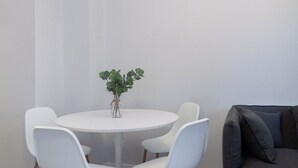Uma sala de jantar com mesa redonda, quatro cadeiras brancas, uma pequena planta e um lustre moderno.