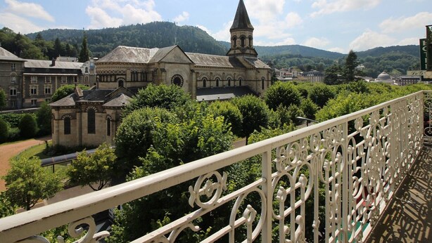 A historic building with a prominent tower, surrounded by lush greenery and a clear sky.
