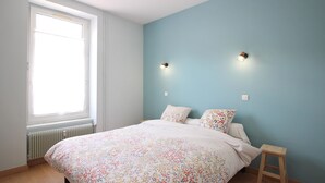 A bedroom with a large bed, two wall-mounted lights, a window, and a radiator.