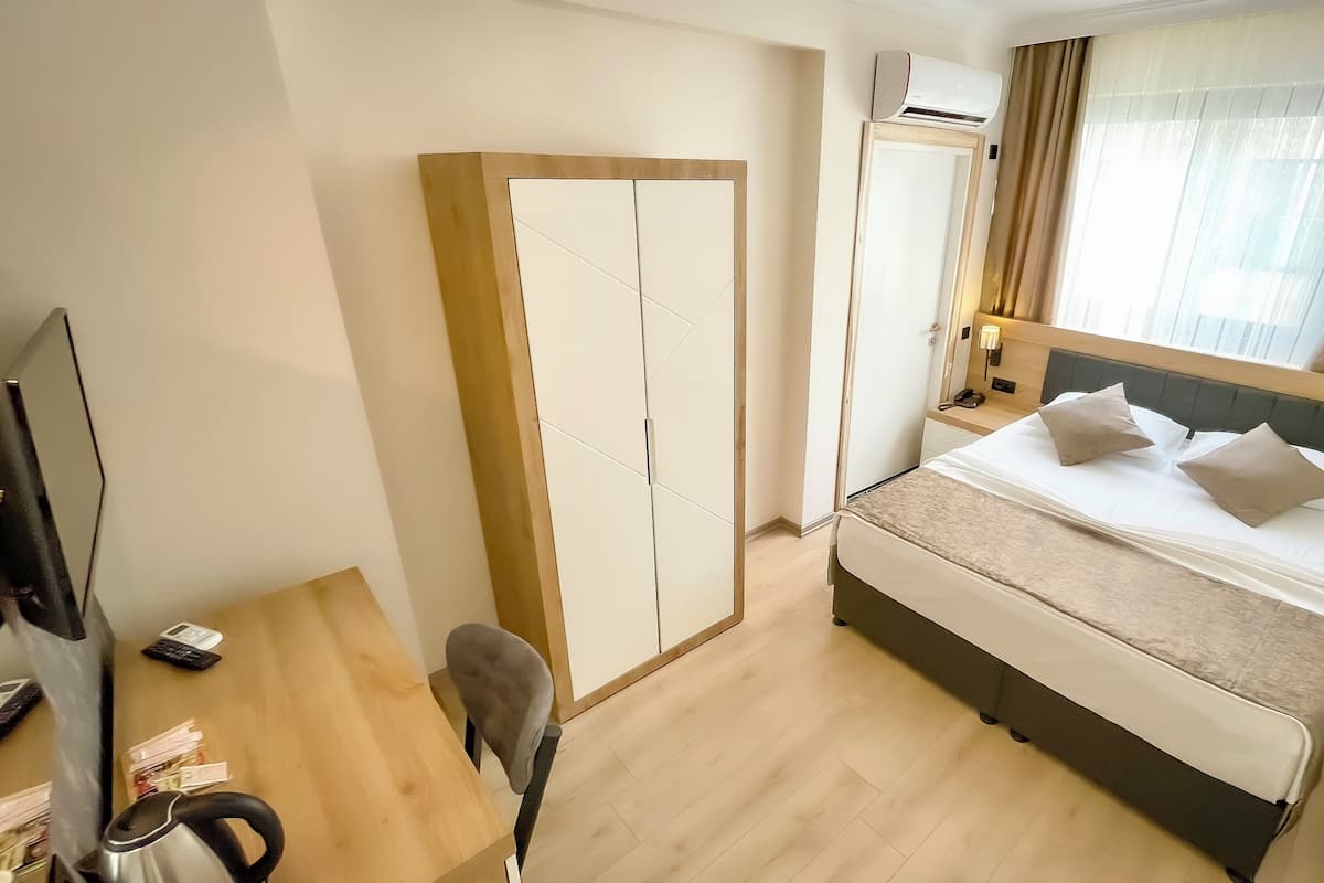 A hotel room with a bed, a wardrobe, a desk, a chair, and a television.