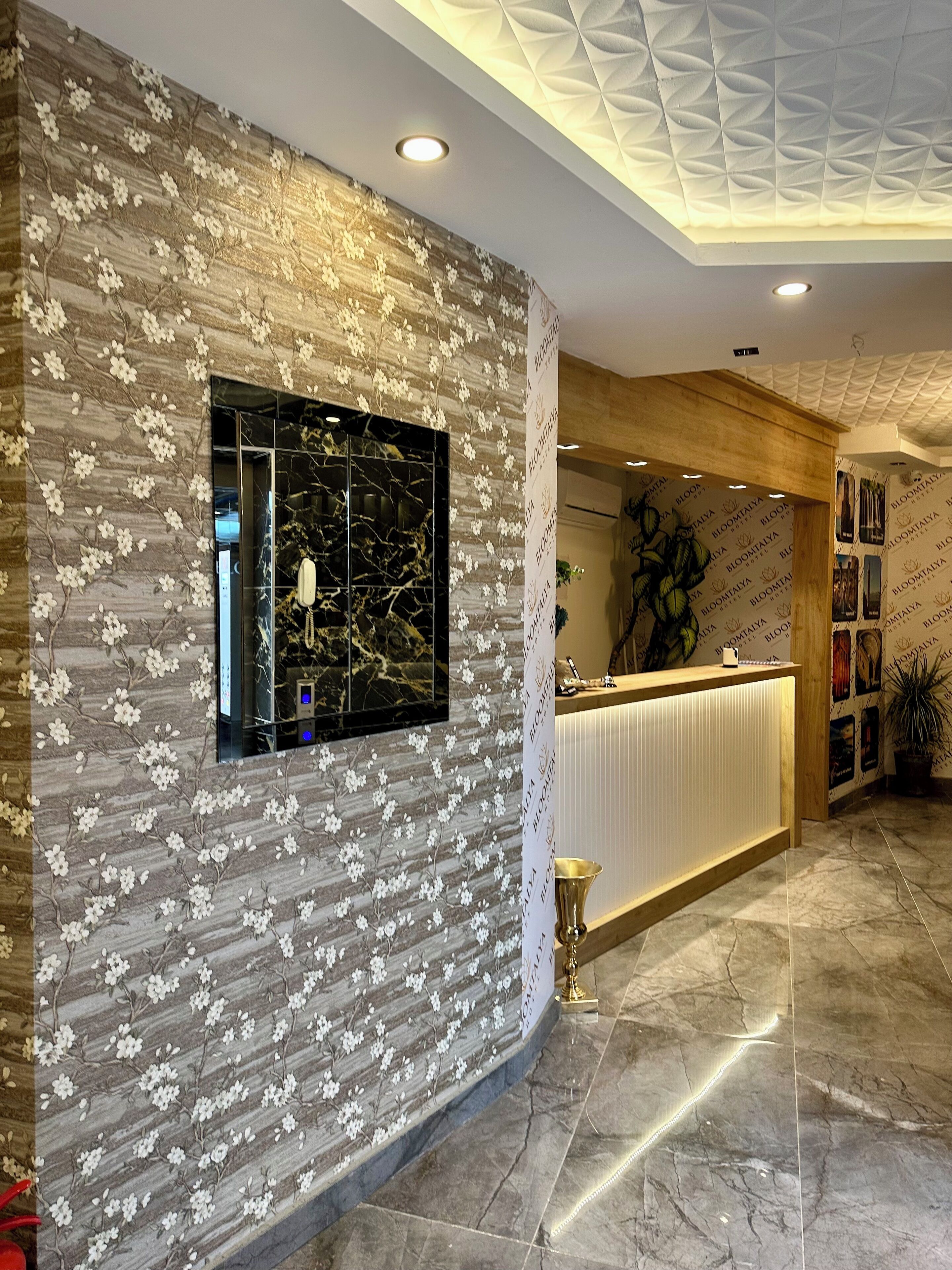 A hotel reception area with a floral wall design, a marble-tiled floor, and a wooden reception desk.