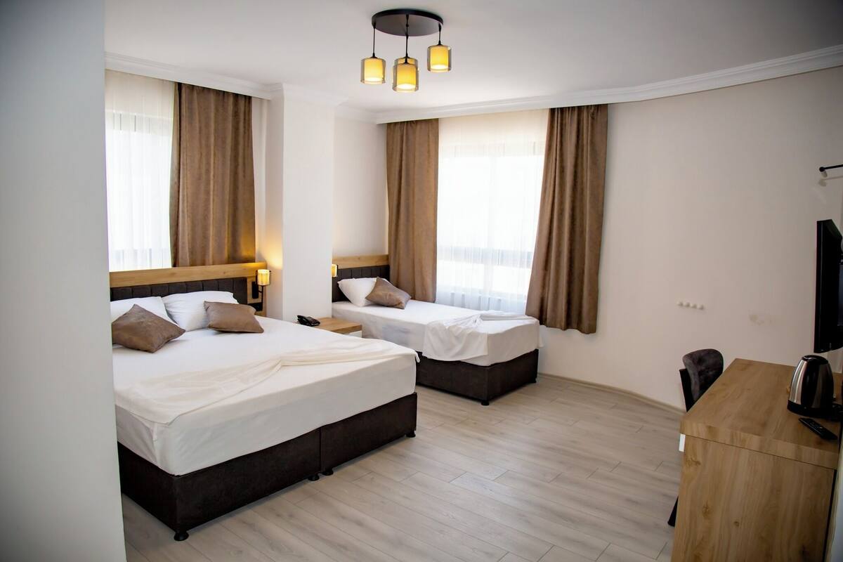 A hotel room with two beds, a wooden desk, a television, and a ceiling light fixture.