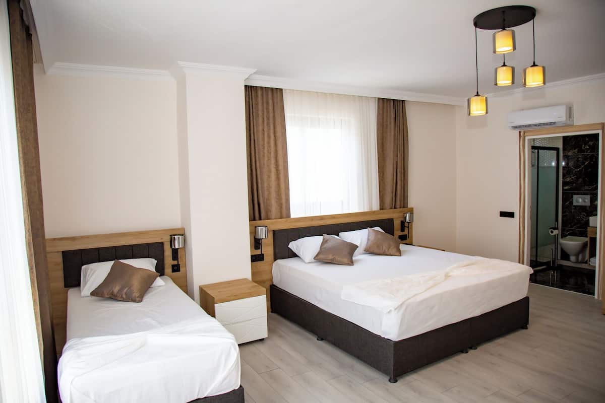 A hotel room with two beds, a wooden headboard, a nightstand, a wall-mounted lamp, and a bathroom visible through an open door.