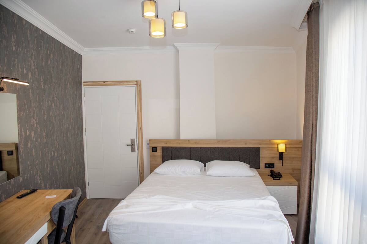 A hotel room with a bed, bedside table, lamp, and a desk with a chair.