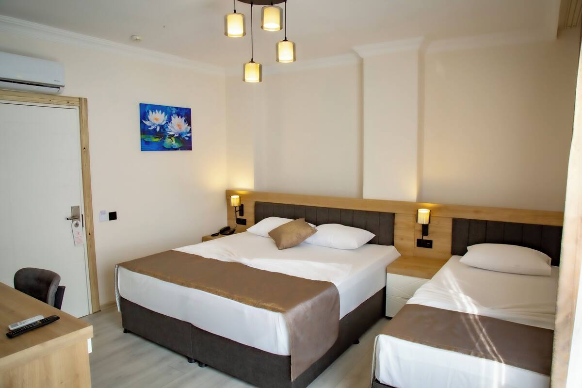 A hotel room with a large bed, bedside tables, a desk, and a painting of flowers.
