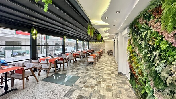 A restaurant with a long counter, multiple tables, and chairs, featuring a patterned tile floor and a wall with green plants. - Bloomtalya Hotel  (Antalya)