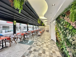 A restaurant with a long counter, multiple tables, and chairs, featuring a patterned tile floor and a wall with green plants. - Bloomtalya Hotel  (Antalya)