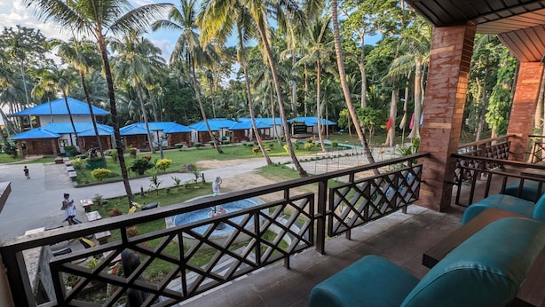 A view from a balcony overlooking a resort with multiple blue-roofed buildings, a swimming pool, and lush greenery. - Pearl Park Beach Resort Private Limited (Port Blair)